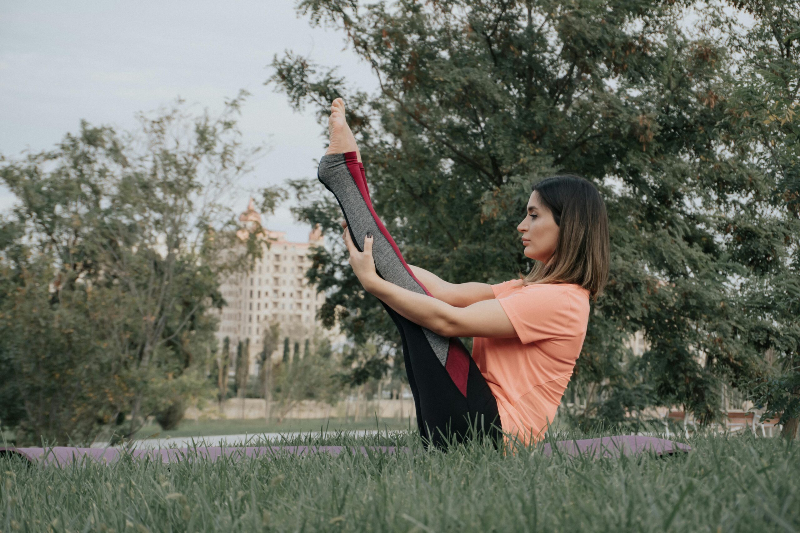 Eine Frau f&Atilde;&frac14;hrt in einer ruhigen Parkumgebung auf Gras Yoga-&Atilde;œbungen durch und f&Atilde;&para;rdert so Achtsamkeit und Fitness.